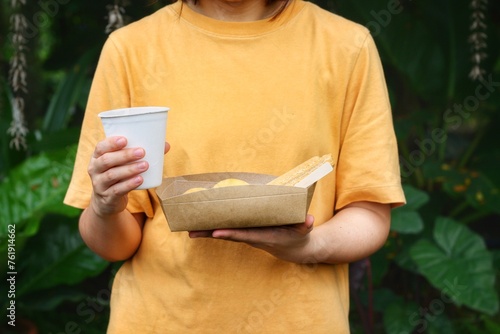 Photos Young girl is showing disposable bagasse coffee cup and paper packaging for takeaway food or drink in hand