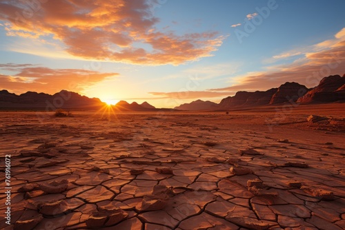 Sun setting over cracked desert with mountains in background