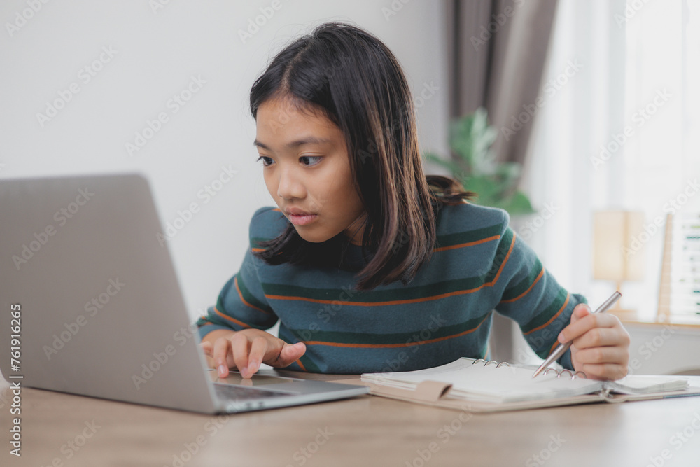 A girl is sitting at a desk with a laptop and a notebook A girl is sitting at a desk with a laptop and a notebook