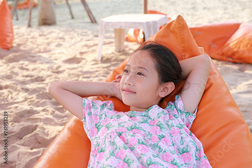 Closeup of smiling Asian young girl relax on orange sofa bed beach on sand at summer holiday.