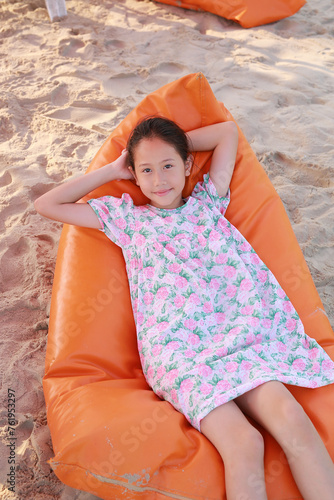 Portrait of smiling Asian young girl relax on sofa bed beach on sand at summer holiday.