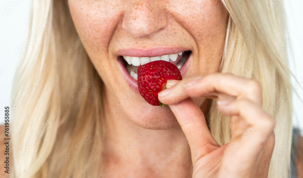 Blonde woman with freckles smiling biting on a strawberry Blonde woman with freckles smiling biting on a strawberry