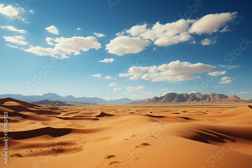 A natural landscape with mountains, sand, and cumulus clouds under a blue sky