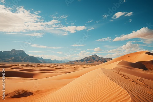 Vast desert landscape with sand dunes, mountains, and cloudy sky on the horizon
