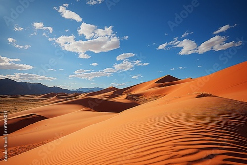 Sand dunes in the desert with mountains in the background under a clear sky