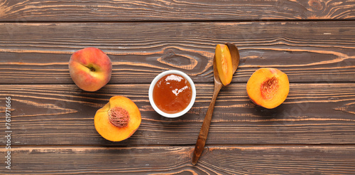 Bowl of sweet peach jam, spoon and fresh fruit on wooden background, top view