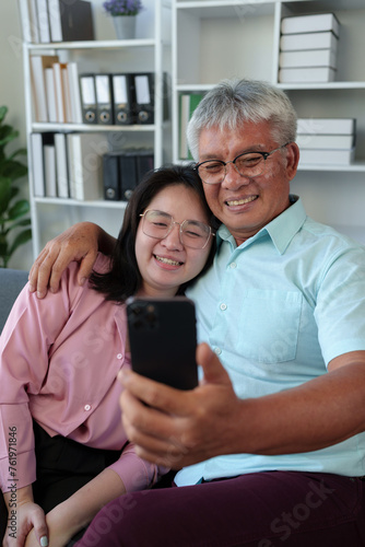Senior Asian father and daughter having an online video call, chatting, greeting, taking selfies happily. Popular online businesses on smartphones Warm morning at home family life concept.