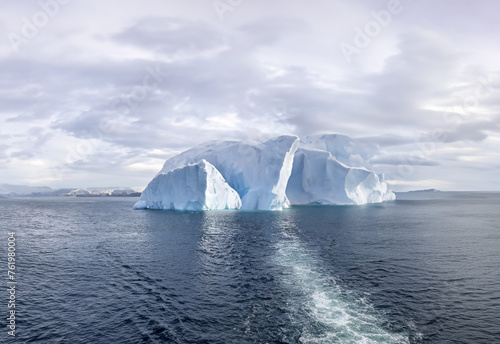 A giant white iceberg drifts in a cold blue sea under a cloudy winter sky