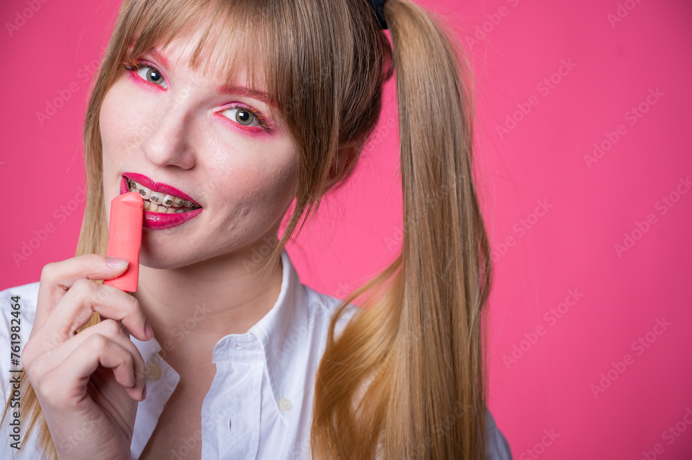 Portrait of a young woman with braces and bright makeup chewing gum on a pink background. Portrait of a young woman with braces and bright makeup chewing gum on a pink background.