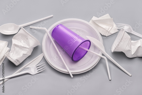 Used plastic utensils, crumpled disposable cups and paper napkins on a gray background. Plastic recycling.