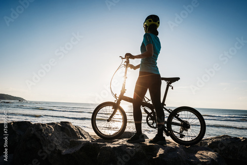 Woman taking a folding bike on sunrise seaside