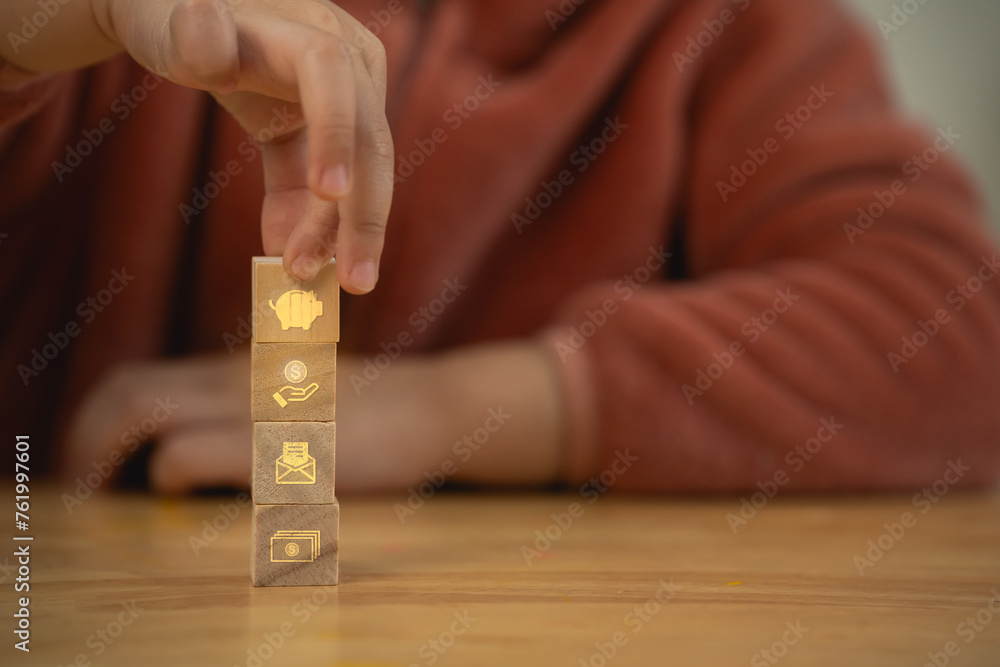 A person holding a stack of wooden blocks with a gold virtual icon about save money planning. The blocks have different symbols on money management finance concept.