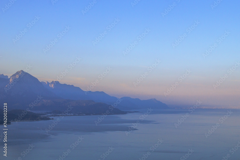 Tranquil seascape with distant mountain range, clear blue sky, and serene atmosphere.