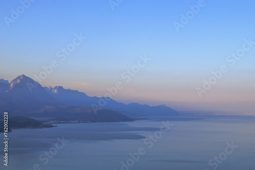 Tranquil seascape with distant mountain range, clear blue sky, and serene atmosphere.