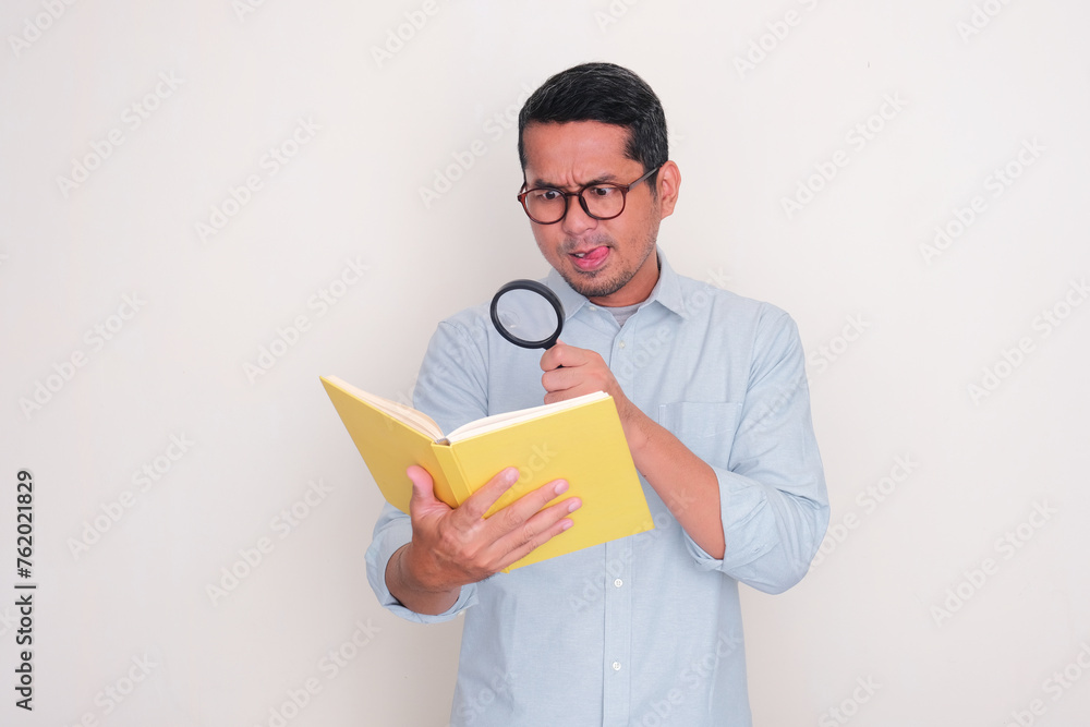 Adult Asian man searching something inside a book using magnifying glass Adult Asian man searching something inside a book using magnifying glass