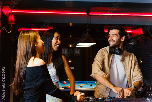 Group of energetic women dancing friends with DJ enjoying night party. Young women dance and hold a wine glass in nightclub. Nightlife, disco dance and girl's night party concept. Fun music festival