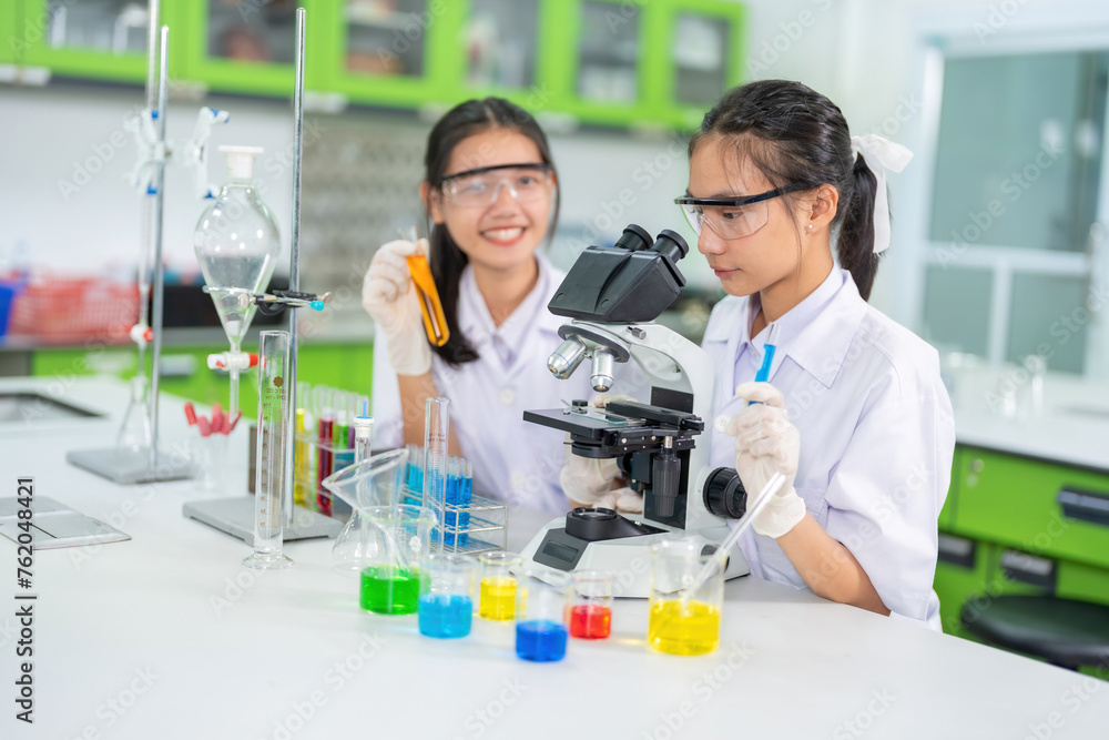 Two female scientists, a student, use a microscope to research a vaccine. On the table are beakers, experimental equipment, holding solution tubes. In the hospital lab Used for medicine Two female scientists, a student, use a microscope to research a vaccine. On the table are beakers, experimental equipment, holding solution tubes. In the hospital lab Used for medicine
