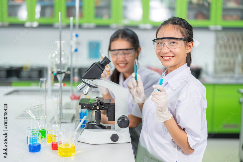 College laboratory of two female scientists using chemical test tubes and a microscope. Produces medicines for treating viruses and COVID vaccines, has beakers and experimental equipment.