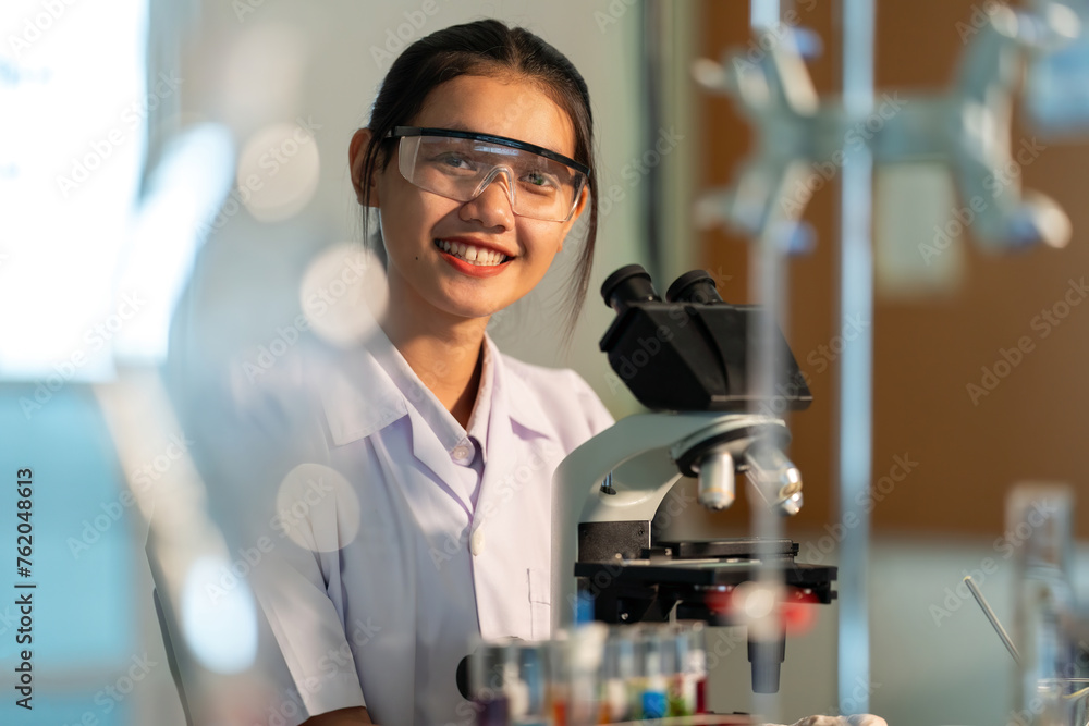 Poster and website image, beautiful smiling Asian female chemist researching cells, using a microscope in a bio-lab of the Ministry of Science, working in a business company, medical industry. Poster and website image, beautiful smiling Asian female chemist researching cells, using a microscope in a bio-lab of the Ministry of Science, working in a business company, medical industry.