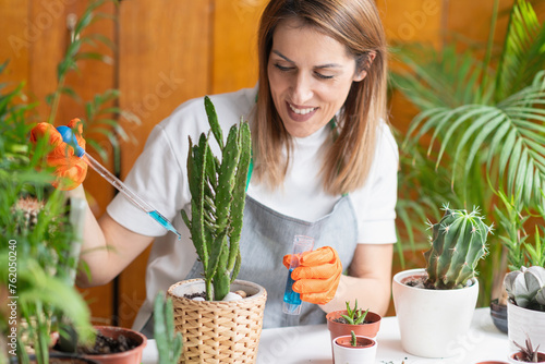 A woman gives special attention to her cactus, carefully fertilizing it at home to ensure healthy growth © Microgen
