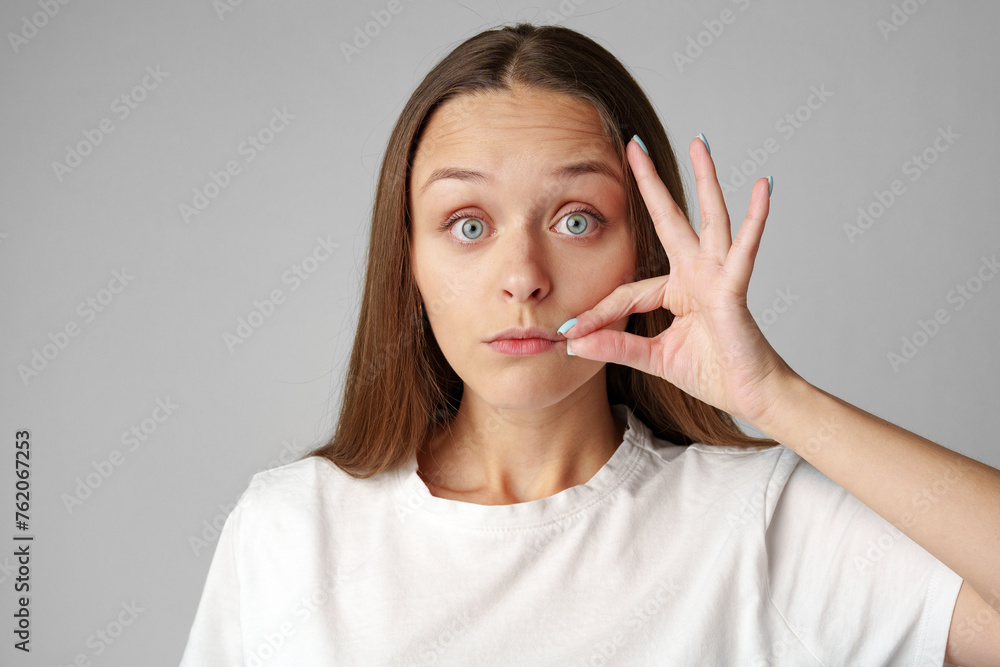 Young pretty woman saying hush be quiet hand sign on gray background Young pretty woman saying hush be quiet hand sign on gray background
