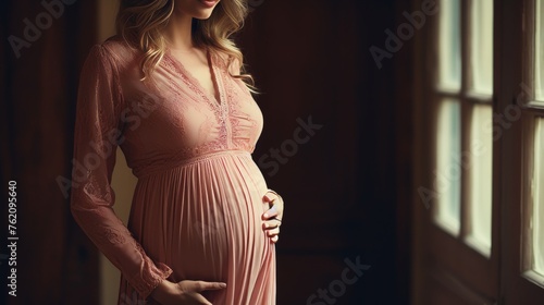 Closeup of pretty young pregnant woman in elegant pink textile clothes showcasing pregnancy belly