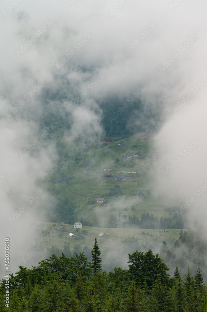 Dense fog in the mountains, through which the houses and the village are barely visible.