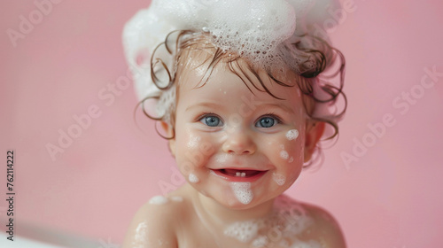 Happy smiling baby with shampoo foamy head on pink background