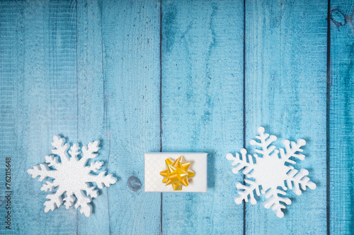 Snowflakes and a present with yellow ribbon on a light blue wooden background. Christmas winter flatlay with copyspace