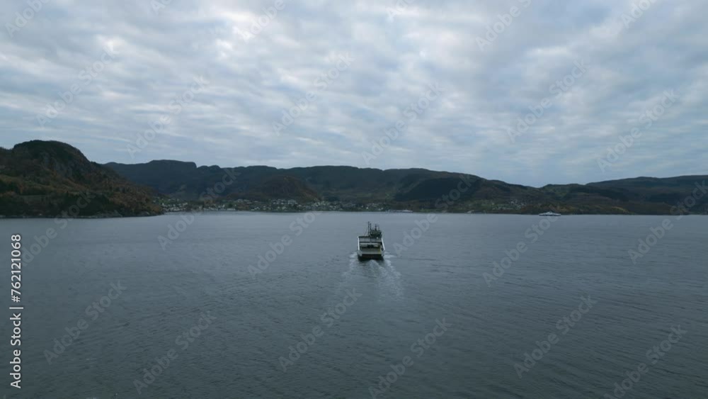 A ferry crossing calm waters near nesvik with hjelmeland backdrop, cloudy skies, aerial view A ferry crossing calm waters near nesvik with hjelmeland backdrop, cloudy skies, aerial view