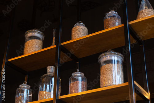 Various types of malting malt in glass pots on a wooden shelves.