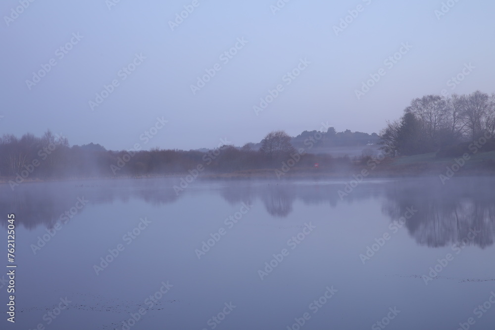 Tranquil lake with mist over water and distant trees
