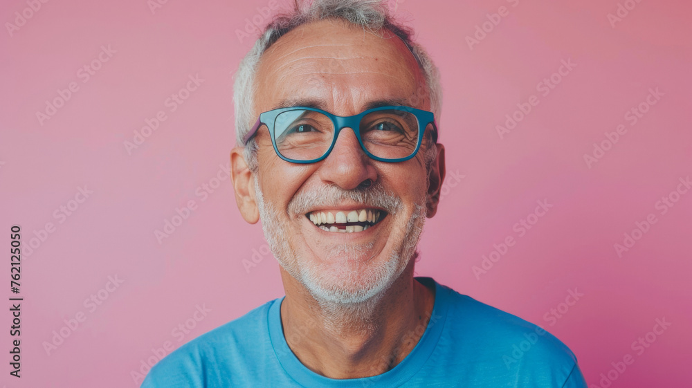 Joyful senior man with blue glasses against a vibrant pink background.