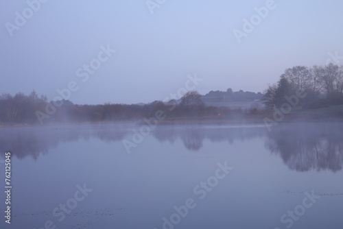 Tranquil lake with mist over water and distant trees © Wirestock
