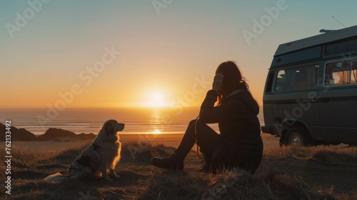 Woman enjoys sunset with her dog near a camper van by the ocean.