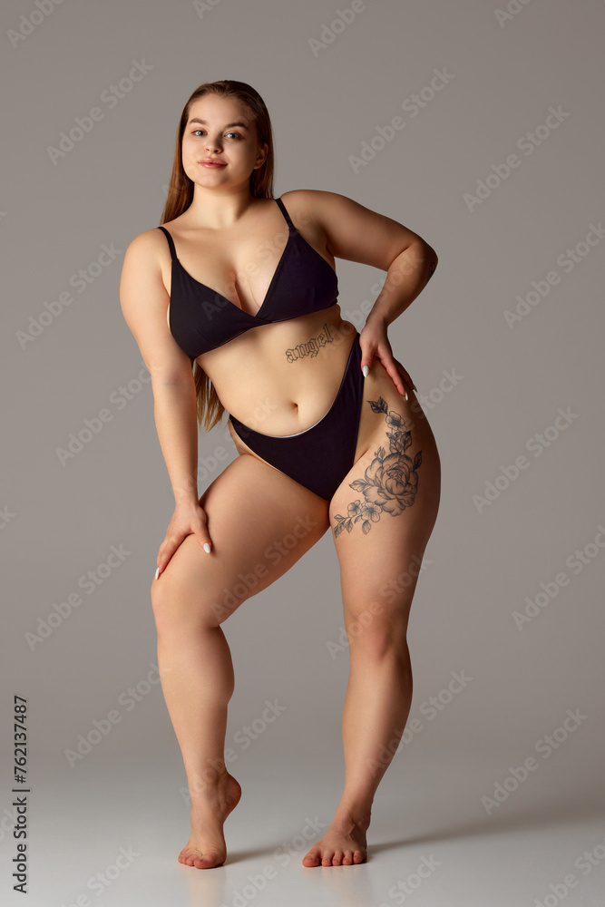 Full length portrait of young chubby woman posing in lingerie against grey studio background. Self-expression. Concept of natural beauty, femininity, body positivity, dieting, fitness, lose-weight. - obrazy, fototapety, plakaty 