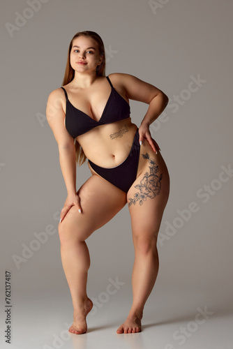 Full length portrait of young chubby woman posing in lingerie against grey studio background. Self-expression. Concept of natural beauty, femininity, body positivity, dieting, fitness, lose-weight.