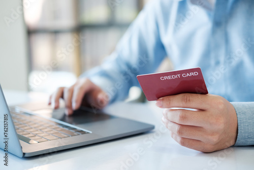 A man is using a laptop to pay for something with a red credit card
