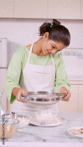 vertical shot of happy smiling Indian household woman preparing flour for making chapati at kitchen - concept of responsibility, healthy eating and food preparation