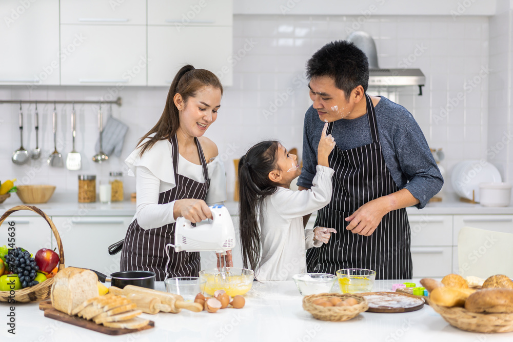 Portrait of enjoy happy love asian family father and mother with little asian girl daughter child play and having fun cooking food together with baking cookie and cake ingredient in kitchen