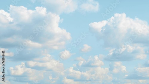 Blue sky covered with slowly moving white clouds. A bright landscape with cumulus clouds floating from left to right.