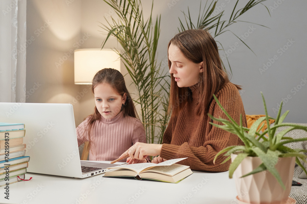Online learning session. Family webinar participation. Remote schooling assistance. Young mother and daughter using laptop in home interior doing homework together Online learning session. Family webinar participation. Remote schooling assistance. Young mother and daughter using laptop in home interior doing homework together
