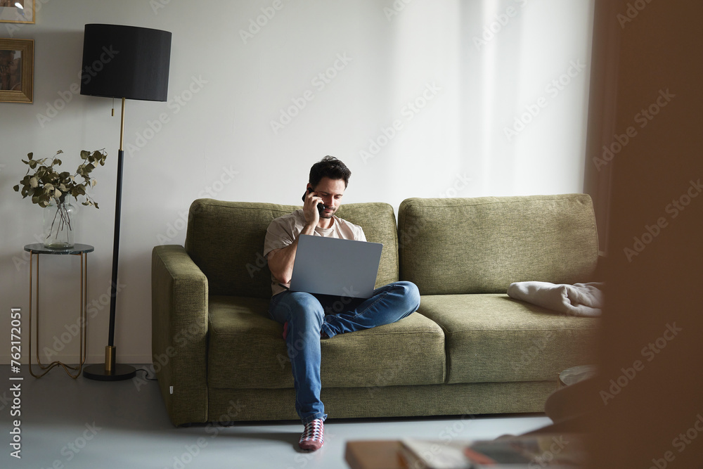 Man using laptop and calling while sitting on sofa Man using laptop and calling while sitting on sofa
