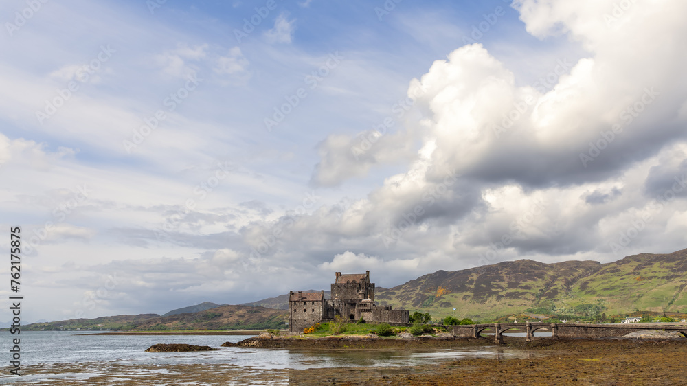 Against a dramatic sky, Eilean Donan Castle's timeless silhouette on the loch's shore is connected to the land by a stone bridge, echoing Scotland's rich past
