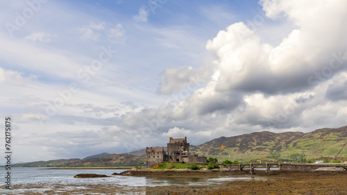 Against a dramatic sky  Eilean Donan Castle s timeless silhouette on the loch s shore is connected to the land by a stone bridge  echoing Scotland s rich past