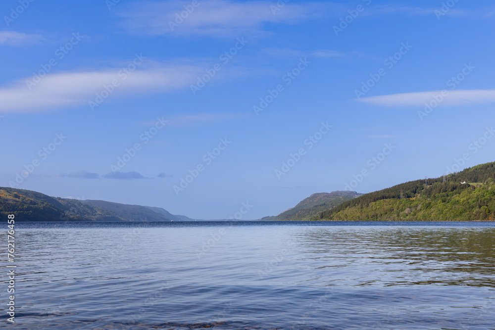 The calm waters of Loch Ness stretch towards the horizon, framed by verdant, forested hills under a vast sky. This iconic Scottish lake invites contemplation and exploration The calm waters of Loch Ness stretch towards the horizon, framed by verdant, forested hills under a vast sky. This iconic Scottish lake invites contemplation and exploration