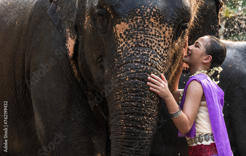 Young pretty Thai woman in colorful traditional Thai costume with friendly elephant in elephant sanctuary, woman and elephant relationship concept