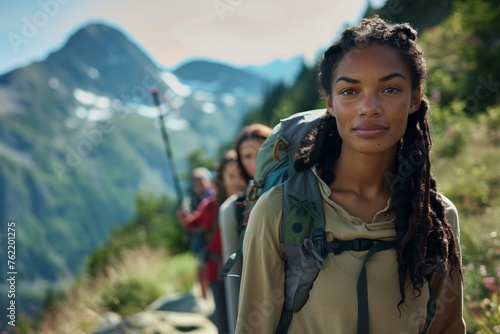 Portrait of a young biracial woman leading a group of hikers on the mountain trail looking at camera.