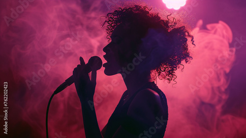Silhouette of curly haired woman singing with microphone on stage © IgnacioJulian