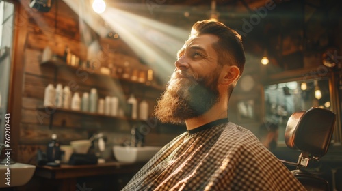 A man with a beard sits in a barber chair with a smile on his face. The barber shop is filled with various bottles and bottles of hair products, including a bottle of shampoo photo